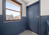 Thumbnail 9 of 30 - A room with a blue door and a window showing a view of a building outside.