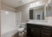 Thumbnail 10 of 15 - A white toilet sits in a bathroom with a white tub and sink.
