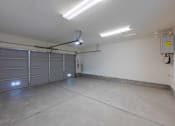 Thumbnail 15 of 15 - A spacious garage with a closed grey door and a fire extinguisher mounted on the wall.