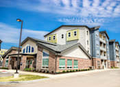 Thumbnail 11 of 34 - A large apartment complex with multiple buildings and a parking lot in front.