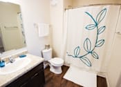 Thumbnail 26 of 34 - A bathroom with a white toilet and a shower curtain with blue leaves on it.