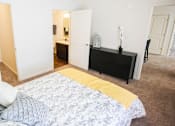 Thumbnail 23 of 34 - A bed with a yellow blanket is in the foreground of a room with a dresser and mirror.