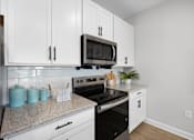 Thumbnail 8 of 83 - A kitchen with white cabinets and a black microwave above the stove.
