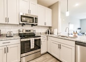 Thumbnail 56 of 94 - a kitchen with stainless steel appliances and white cabinets at Vantage Luxury Apartments in  Cape Coral, FL