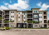 Thumbnail 19 of 94 - an apartment building with a parking lot and a green car in front of it
