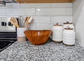 Thumbnail 14 of 51 - A kitchen counter with a wooden bowl, white ceramic jars, and utensils.