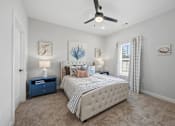 Thumbnail 23 of 51 - A bedroom with a large bed, a ceiling fan, and a nightstand with a lamp.