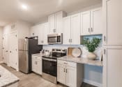Thumbnail 22 of 57 - a kitchen with white cabinets and stainless steel appliances at  a living room with tables and chairs and a ceiling fan at Swiftwater luxury apartments in Port Charlotte, FL