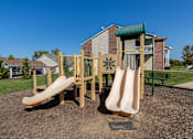 Thumbnail 40 of 43 - A playground with a slide and a green roofed building in the background.