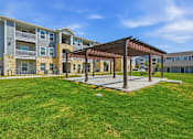 Thumbnail 6 of 45 - A sunny day at a grassy courtyard with a wooden pavilion and apartment buildings in the background.