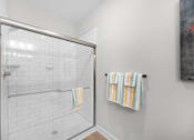 Thumbnail 26 of 83 - A white tiled shower with a glass door and a towel rack with two towels hanging on it.
