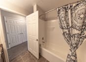 Thumbnail 5 of 43 - A bathroom with a bathtub, shower curtain, and two doors.