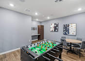 Thumbnail 19 of 45 - A foosball table is in the middle of a room with a dining table and chairs.
