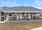 Thumbnail 40 of 58 - A covered picnic area with benches and a playground in the background.
