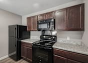 Thumbnail 28 of 45 - A black refrigerator and stove in a kitchen with brown cabinets.