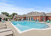 Thumbnail 12 of 34 - A large outdoor swimming pool with lounge chairs and a building in the background.