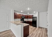 Thumbnail 21 of 34 - A kitchen with a black refrigerator and brown cabinets.