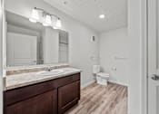 Thumbnail 29 of 34 - A bathroom with a sink, mirror, toilet, and wooden floors.