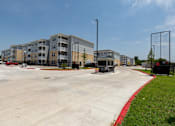 Thumbnail 37 of 39 - A parking lot in front of a multi-story apartment building.