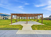 Thumbnail 11 of 45 - A wooden pergola is in the middle of a grassy area.