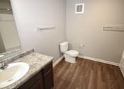 Thumbnail 18 of 25 - A bathroom with a toilet, sink, and wooden floors.