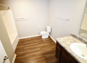 Thumbnail 15 of 25 - A bathroom with a toilet, sink, and wooden floors.