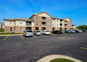 Thumbnail 4 of 15 - a parking lot with cars in front of Canterbury apartment buildings in Kalamazoo, Mi