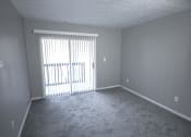 Thumbnail 7 of 11 - Empty living room with white walls and a sliding glass door and a carpeted floor at Canterbury House apartments in Logansport, Indiana
