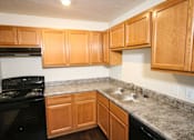 Thumbnail 1 of 18 - A kitchen with wooden cabinets and a black stove top oven.