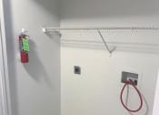 Thumbnail 9 of 18 - Small room with a white wall and a white shelf with a red fire extinguisher at Conner Court apartments in Connersville, IN