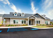 Thumbnail 2 of 42 - Aurora Apartments clubhouse building  with a gray roof and blue handicapped parking spaces