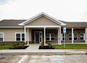 Thumbnail 1 of 25 - A building with a brown roof and a parking lot in front.
