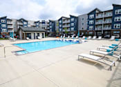 Thumbnail 33 of 34 - A large swimming pool surrounded by lounge chairs in front of apartment buildings.