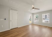 Thumbnail 9 of 50 - A room with a white door, a ceiling fan, and a window showing a parking lot outside.
