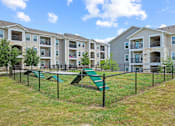 Thumbnail 42 of 50 - A playground area with a green slide and a fence in front of apartment buildings.
