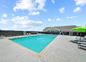 Thumbnail 38 of 50 - A large outdoor swimming pool with a green umbrella and lounge chairs.