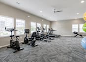 Thumbnail 16 of 21 - A spacious gym with a variety of exercise equipment and a ceiling fan.