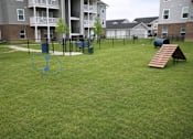 Thumbnail 16 of 20 - A playground with a slide and a seesaw in the middle of a grassy area.