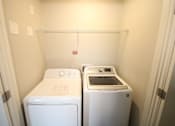 Thumbnail 6 of 20 - Two white front loading washing machines in a small laundry room.
