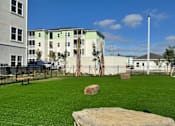 Thumbnail 68 of 83 - A large rock sits in the middle of a grassy area with a building in the background.