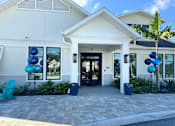 Thumbnail 66 of 83 - A white house with a black door and windows, surrounded by plants and blue balloons.