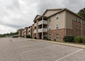 Thumbnail 11 of 24 - A parking lot in front of a brick apartment building.