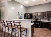 Thumbnail 4 of 31 - Clubhouse kitchen with 3 barstools and cabinets and black appliances at Mosaic Apartments in Avon, Indiana