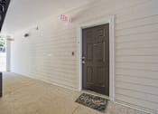 Thumbnail 13 of 33 - A white building with a brown door and a green mat on the floor.