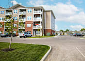 Thumbnail 8 of 15 - A tree stands in a grassy area in front of apartment buildings.