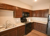 Thumbnail 1 of 15 - A kitchen with dark wood cabinets and black appliances.