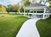 Thumbnail 5 of 15 - A pavement pathway leads to a pavilion with picnic tables.