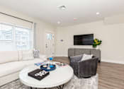 Thumbnail 2 of 31 - A living room with a white couch, a grey armchair, a coffee table with a black book on it, and a flat screen TV mounted on the wall.
