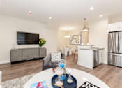 Thumbnail 3 of 31 - A modern living room with a grey sofa, a white coffee table, and a kitchen in the background.