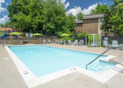 Thumbnail 19 of 28 - a swimming pool with lounge chairs and umbrellas in front of a brick building at Stonewater Apartments, Louisville Kentucky